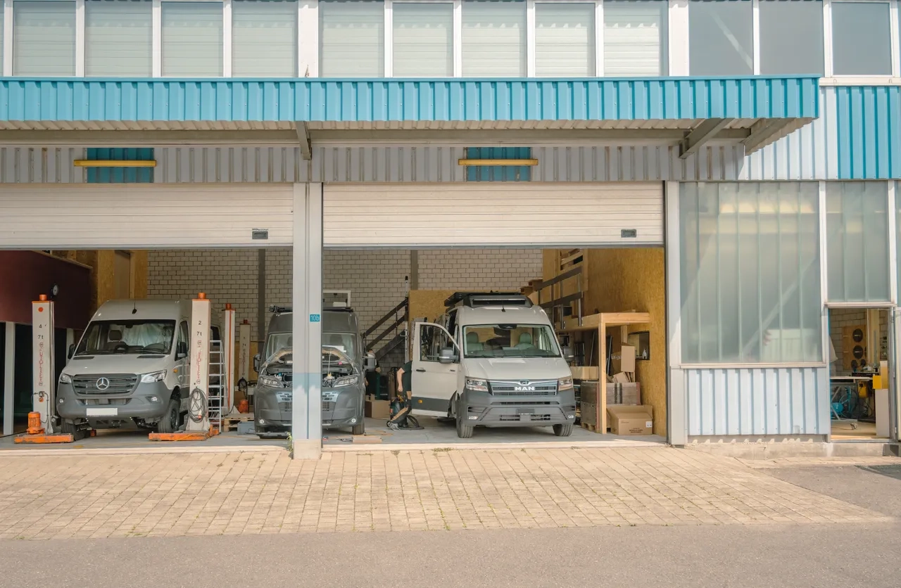 Werkstatt von Cocoon Vans GmbH mit drei Camper Vans und offenen Toren an einem Sommertag