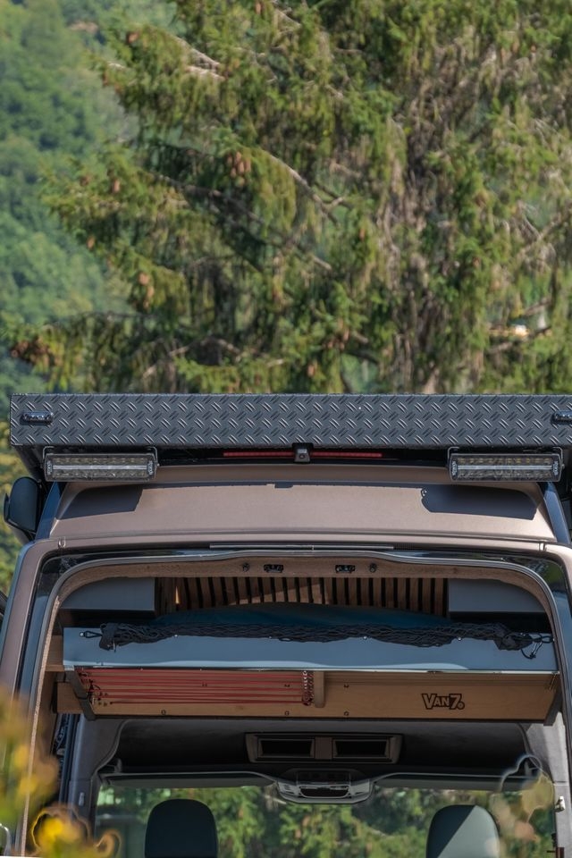 Ein Blick in den VW Crafter 4x4 mit geöffneten Hecktüren. Der Camper Van von Cocoon Vans verfügt über ein Hubbett, der Innenausbau ist aus amerikanischem Nussbaum gefertigt.