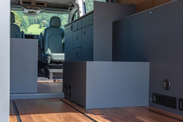 Innenausbau von Cocoon Vans eines VW Crafters 4x4 mit Holzakzenten aus amerikanischem Nussbraum, zwei grünen Ledersitzen, viel Stauraum über Kopf und einem kompakten Küchenbereich.