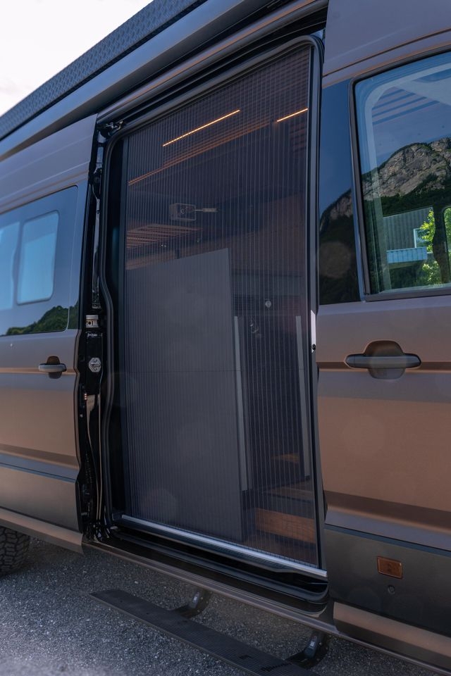 Ausfahrbare Tritt für den Einstieg in den VW Crafter 4x4. Das Fliegengitter an der Seitentür ist geschlossen.